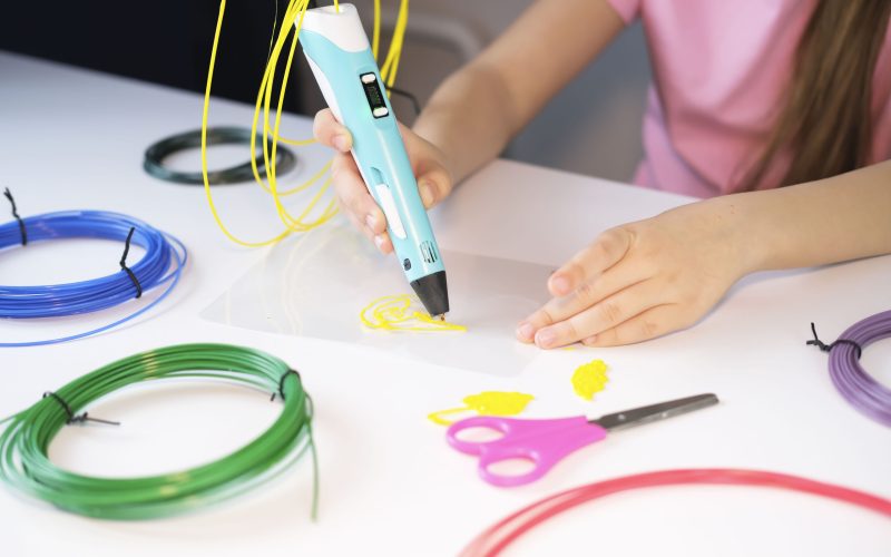 3D printable pen, hands holding colorful toy. Colored plastic in rolls. STEM education. Play and learn at school and at home. New toy for child.